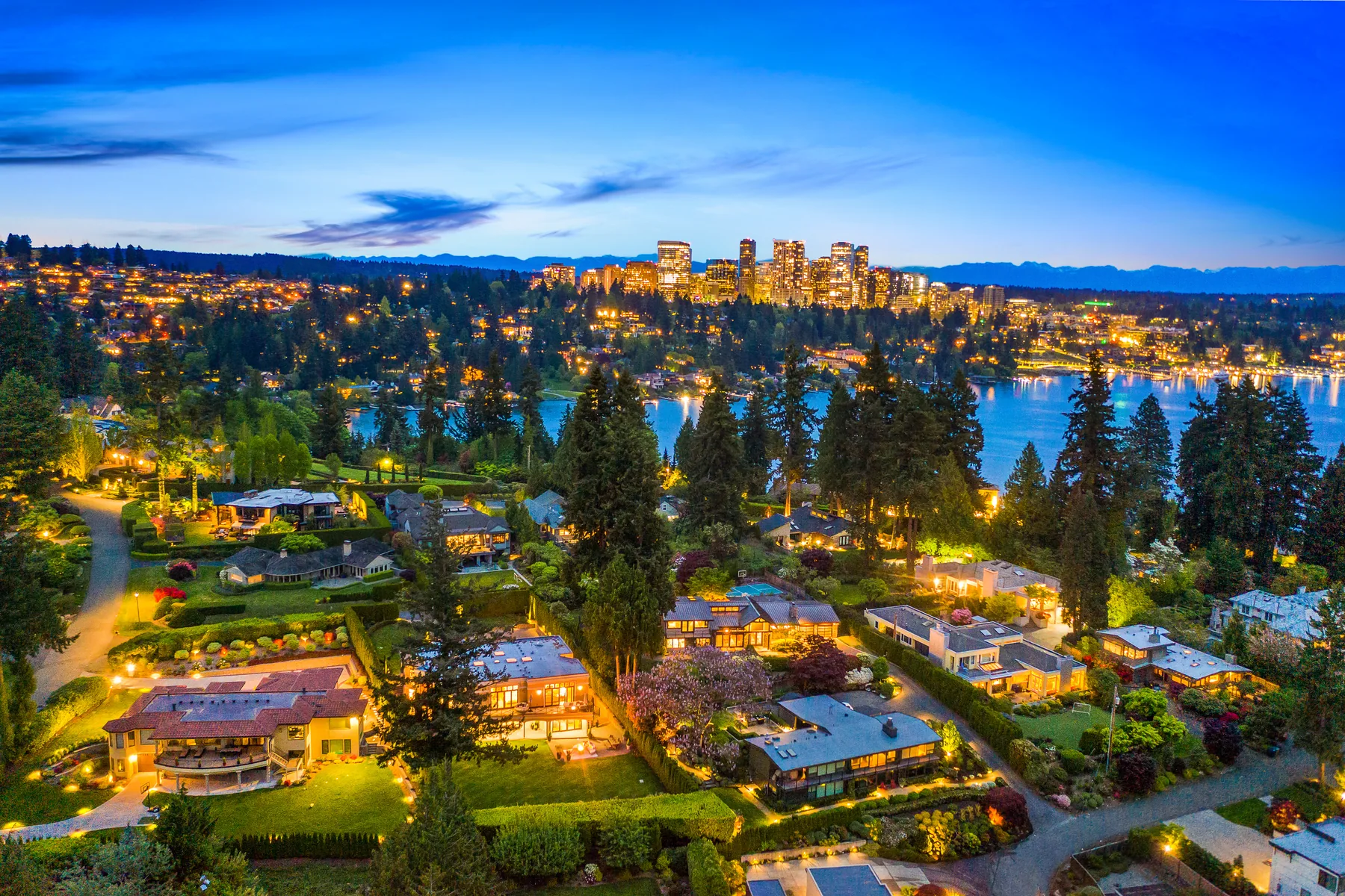 Blue-hour aerial of a lakeside neighborhood and city skyline