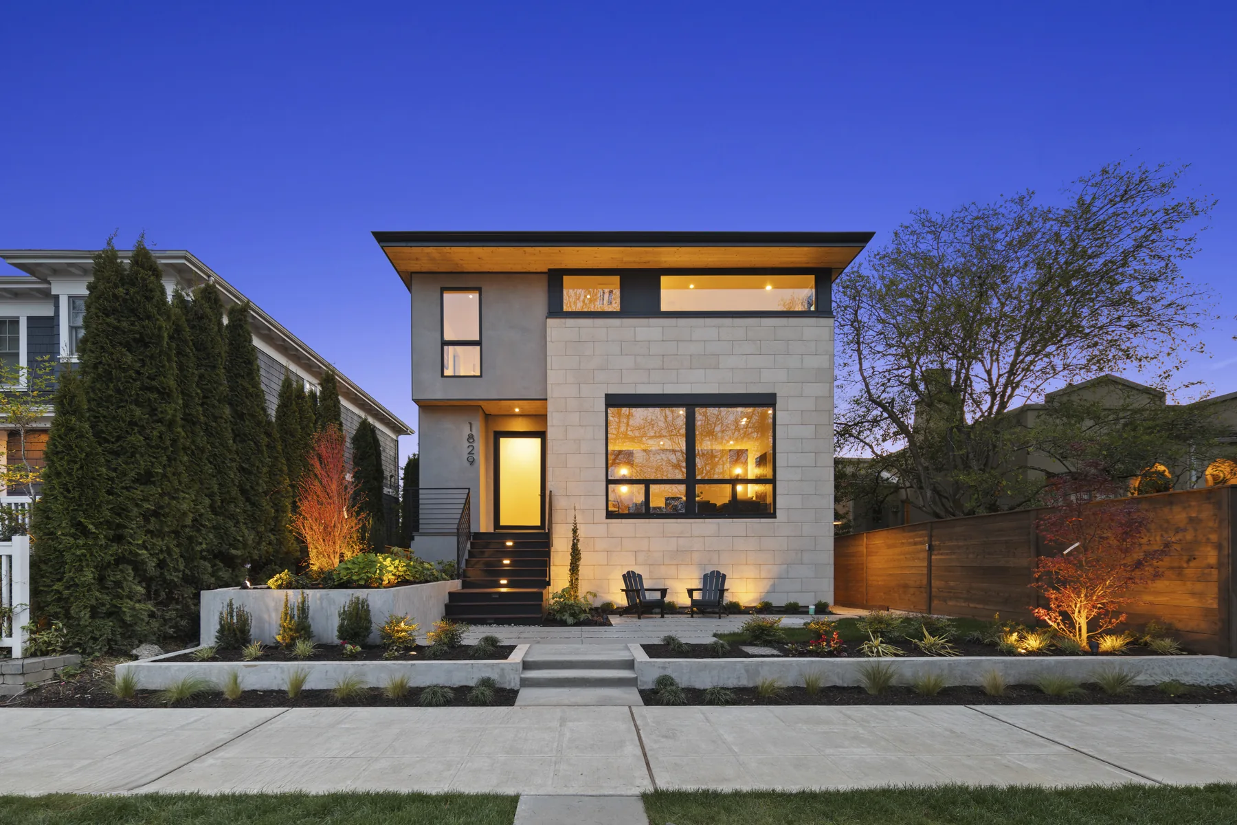Contemporary urban home at blue hour, with warm interior lighting and a landscaped front yard